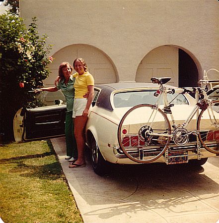 A mother and daughter pose by a car with a bike on the back of it.